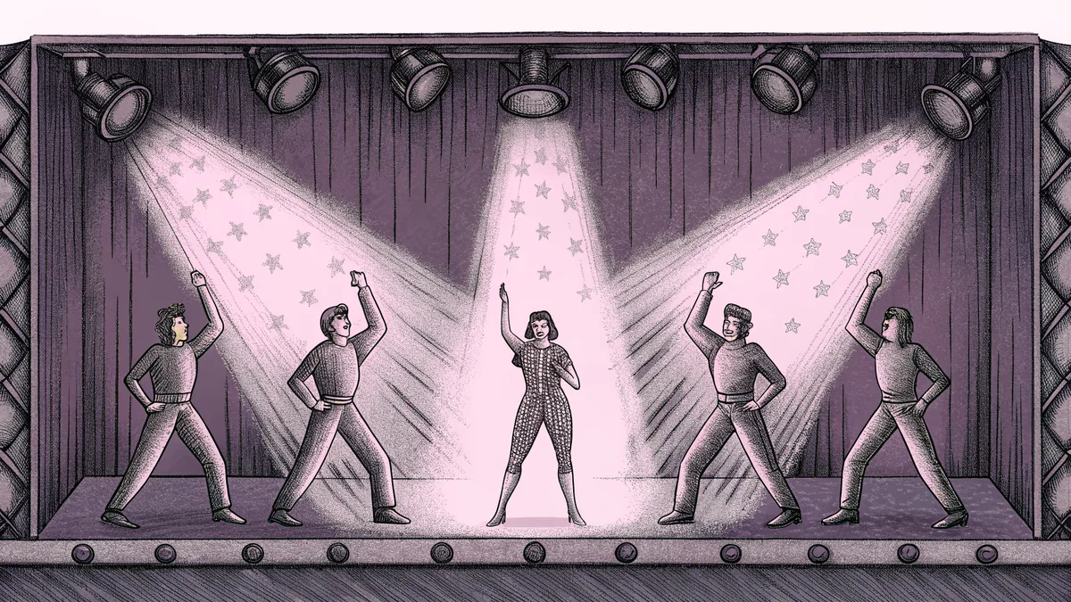 A performer on stage in a sparkling outfit surrounded by stage lighting and dancers.