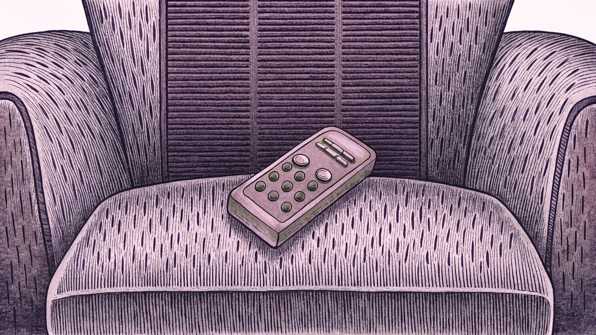 A remote control sits on an armchair beside an old-fashioned rabbit-ear antenna.