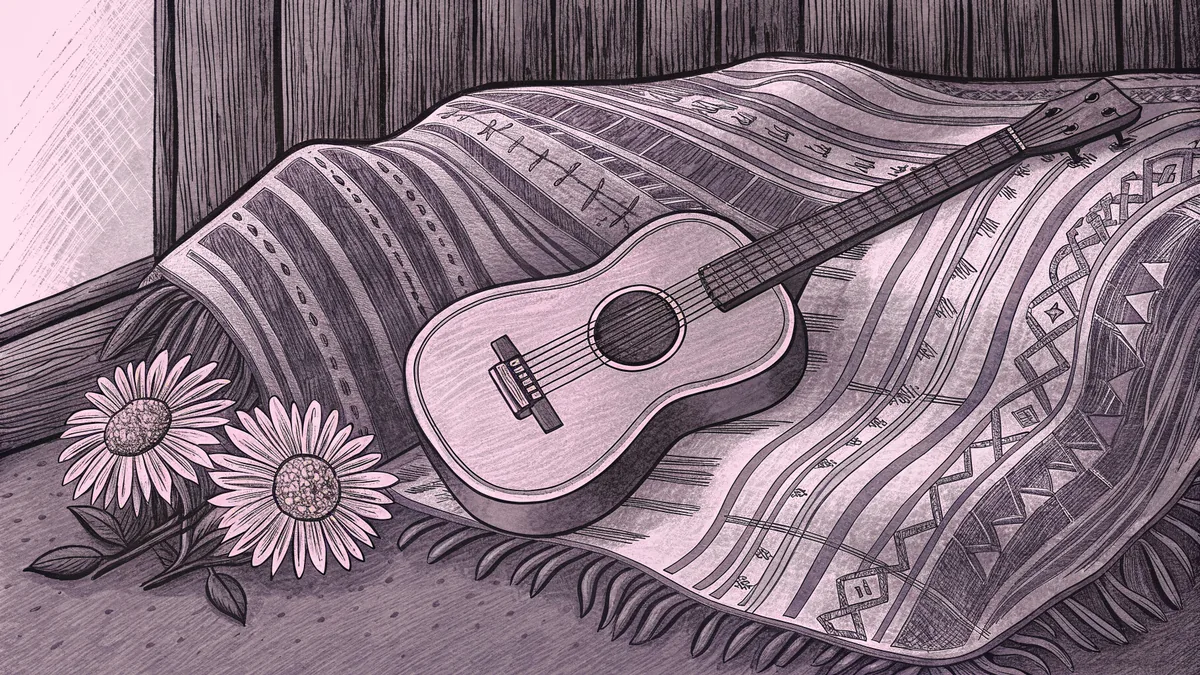 A painted marigold blossom stands beside an acoustic guitar on a woven blanket against a rustic adobe wall.