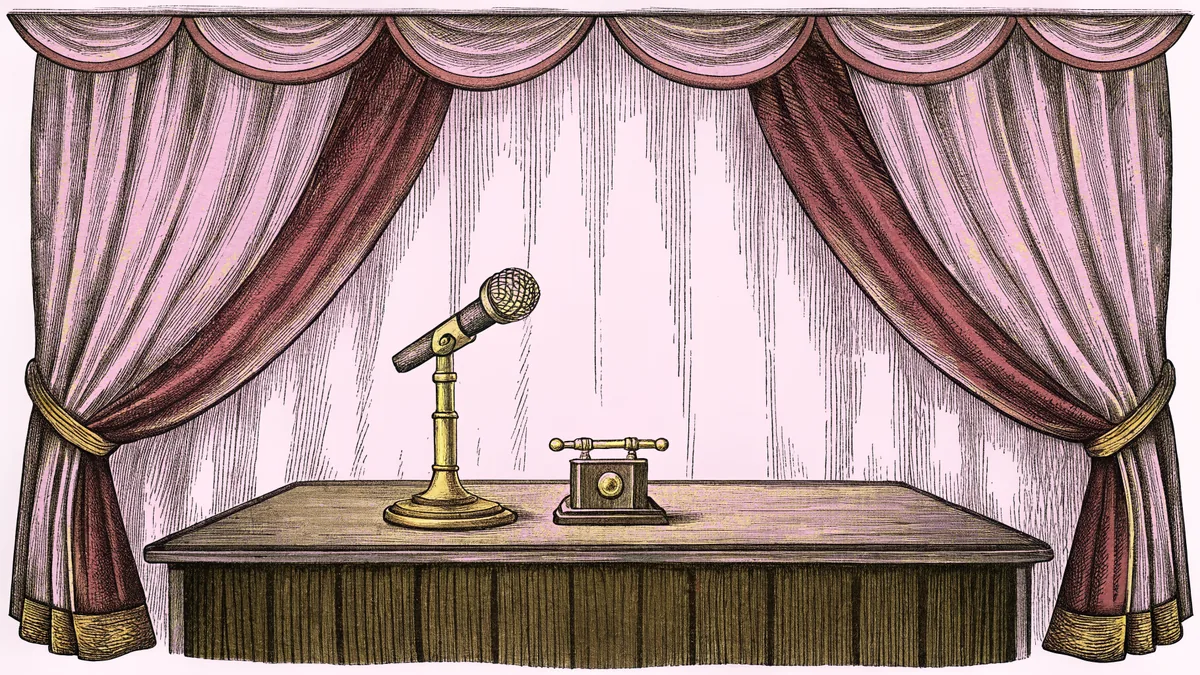 A brass microphone stands beside a candlestick telephone on a wooden broadcast table.