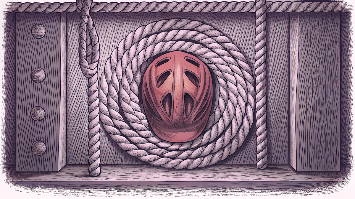 A thick coil of rope beside a red bicycle helmet on wooden planks.