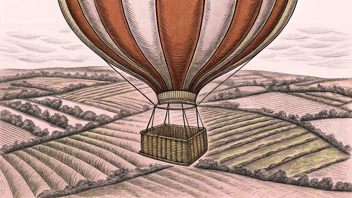 A vibrant hot air balloon rises above farmland with a wicker basket floating beneath.