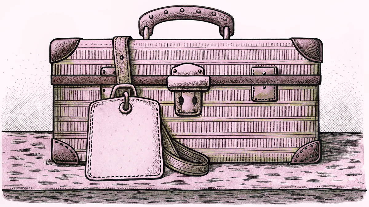 A small hard-shell suitcase with a strap and a plain luggage tag, on a stone counter.