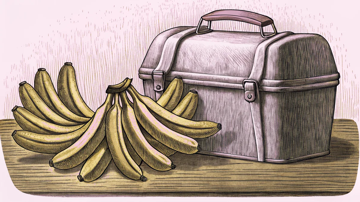 A bunch of bananas resting beside a dented metal lunch pail on a wooden surface.