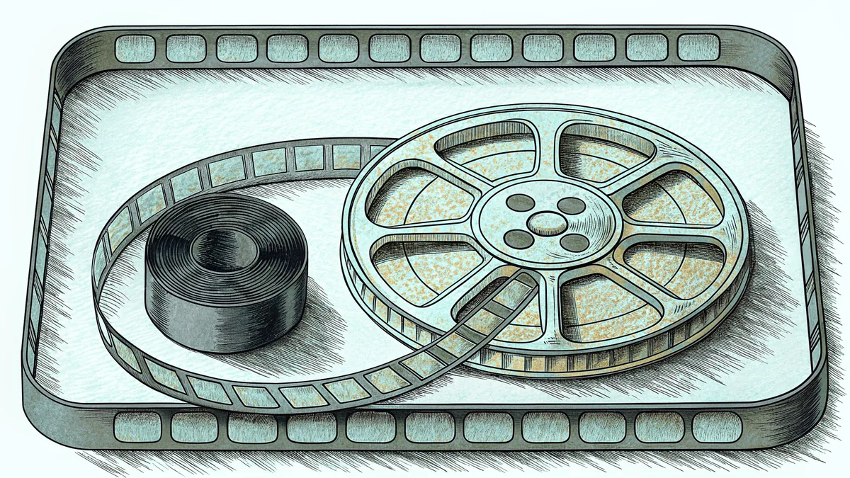 A film reel and a curling strip of film in a shallow tray, beside a tightly wound roll of film.
