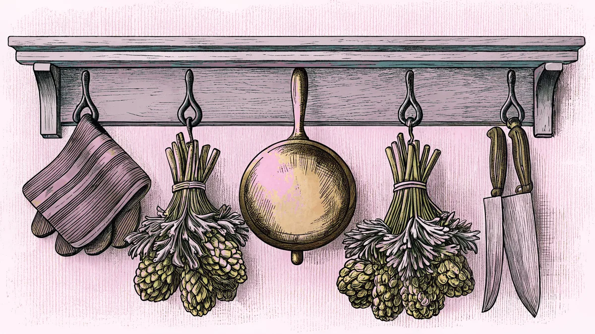 A copper pot hangs above bundled fresh herbs and chef's knives displayed on a wrought-iron bistro shelf.