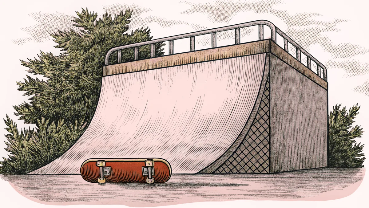 A skateboard with colorful grip tape rests on a concrete ramp with large wheels visible underneath.