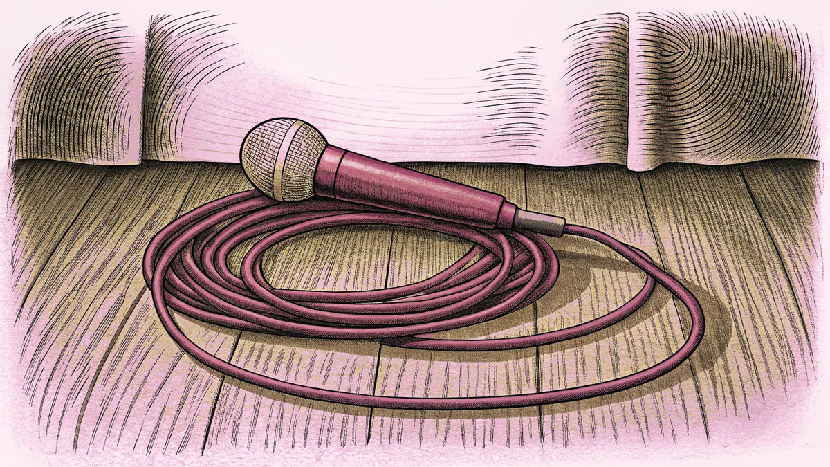 A stage microphone lying beside its coiled cable on a wooden floor, against a pale curved backdrop.