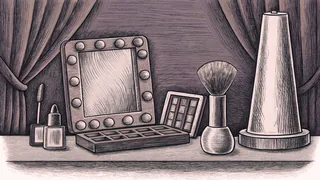 Makeup supplies and brushes arranged in front of a stage mirror with theatrical spot lighting.