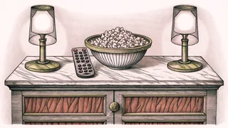 A remote control and popcorn sit on a marble counter beneath vintage spotlights.