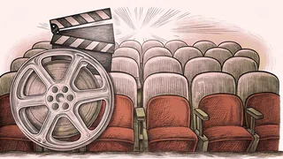 A film canister and clapper board rest on a red cinema seat under a theatrical spotlight.