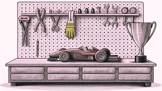 A gleaming model race car sits before a mechanic's tool rack and polished trophy on a workshop shelf.