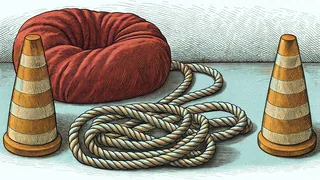 A red beanbag and a knotted tug of war rope rest beside orange obstacle cones on a sunlit field.