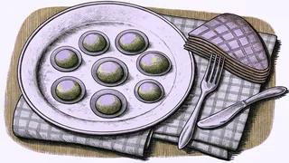 A plate of green eggs and a slice of ham sit beside a fork on a chequered cloth.