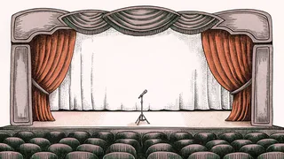 A blank clapper board and camera on a tripod rest on a dimly lit theatre stage.