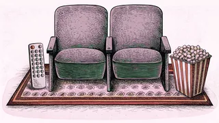 A remote control and popcorn box sit beside a cinema seat row on a rug.