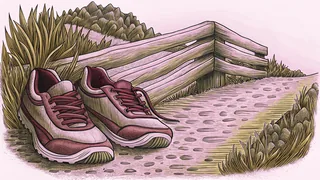 A pair of worn running shoes rests beside a steep trail and a wooden hurdle.