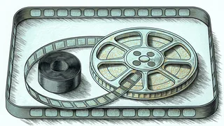 A film reel and a curling strip of film in a shallow tray, beside a tightly wound roll of film.