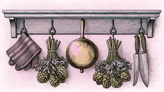 A copper pot hangs above bundled fresh herbs and chef's knives displayed on a wrought-iron bistro shelf.