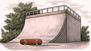 A skateboard with colorful grip tape rests on a concrete ramp with large wheels visible underneath.