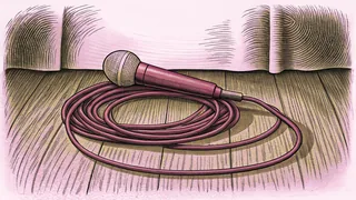 A stage microphone lying beside its coiled cable on a wooden floor, against a pale curved backdrop.