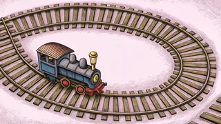 A blue toy steam locomotive stands beside a loop of wooden track and a signal lamp.