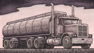 A large semi truck with tanker trailer idles at a truck stop beneath bright overhead lighting.